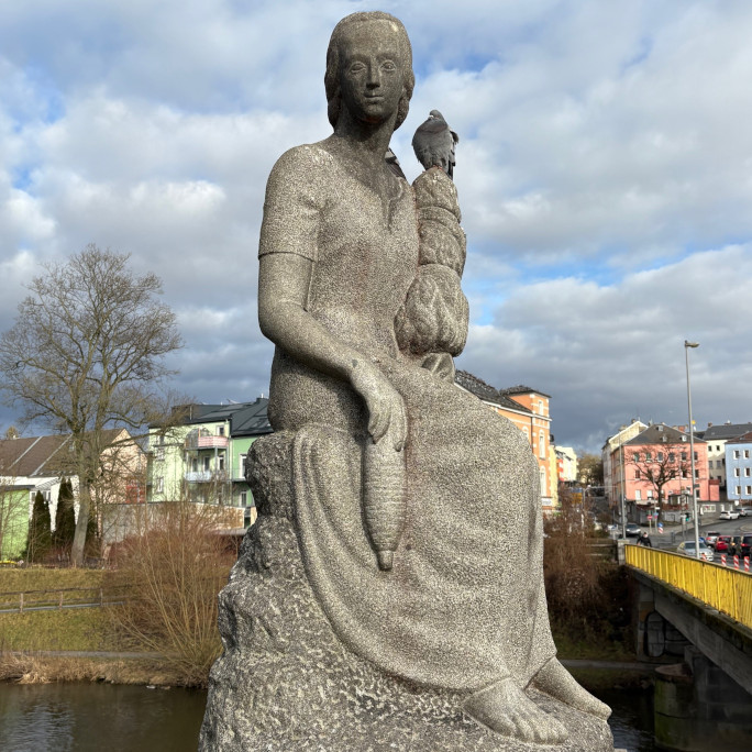 A statue made of stone showing a woman with a spindle, memorial to the long historiy of textile processing in Hof.