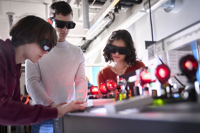 Three young researchers working together in a laboratory with glasses on